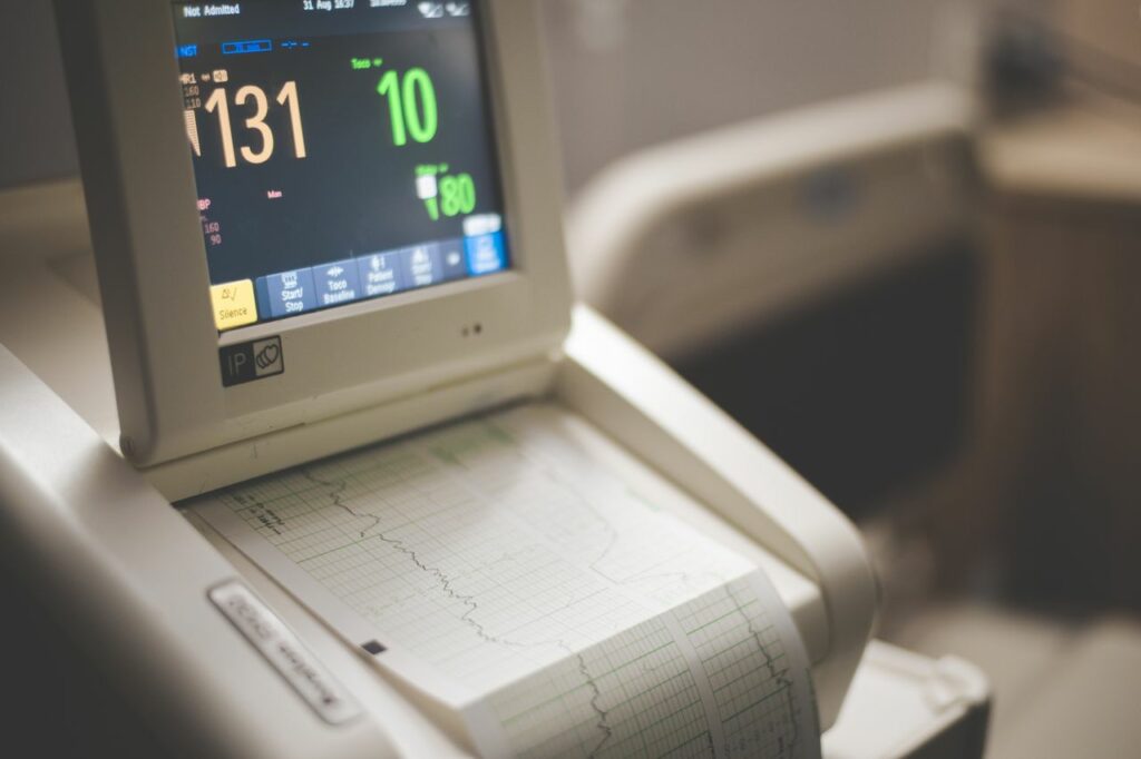 A hospital monitor displays vital signs with a heart rate of 131 and oxygen level of 80; a printed graph of patient data is coming out below the screen.